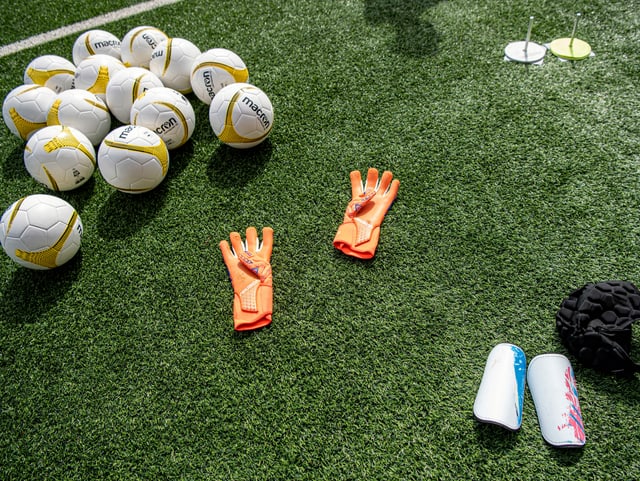 Bälle, Goalie-Handschuhe und Schoner liegen auf dem Rasen. Bälle, Goalie-Handschuhe und Schoner liegen auf dem Rasen.