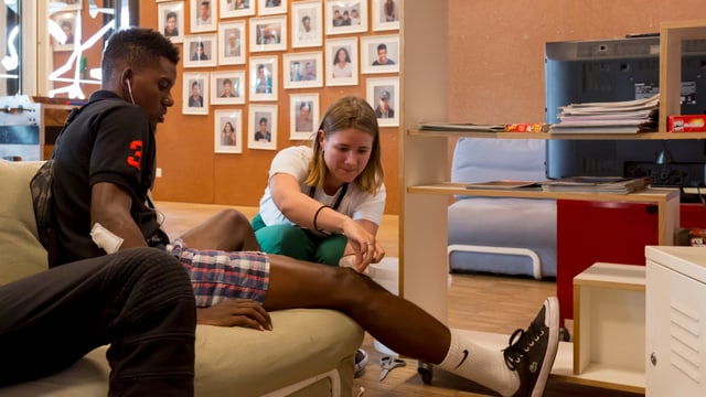Eine Frau klebt einem jungen Mann ein Pflaster aufs Knie. Eine Frau klebt einem jungen Mann ein Pflaster aufs Knie.