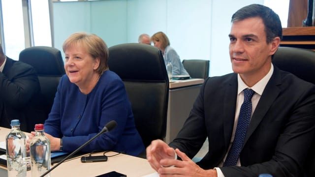 Merkel und Sanchez sitzen an einem Tisch nebeneinander. Merkel und Sanchez sitzen an einem Tisch nebeneinander.