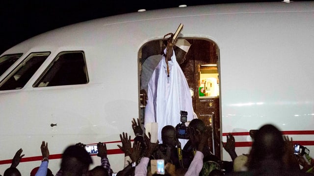 Jammeh in weissem Gewand winkt vom Eingang des Flugzeugs. Jammeh in weissem Gewand winkt vom Eingang des Flugzeugs.