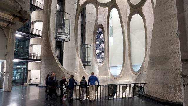 Ein Innenraum aus Beton. Die Wände sind mit runden Löchern geöffnete Röhren in denen gläserne Lifte fahren. Ein Innenraum aus Beton. Die Wände sind mit runden Löchern geöffnete Röhren in denen gläserne Lifte fahren.