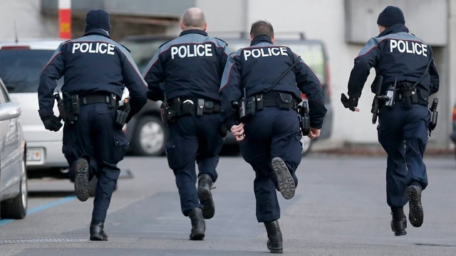 Vier Polizisten (von hinten) rennen eine Strasse entlang. Vier Polizisten (von hinten) rennen eine Strasse entlang.
