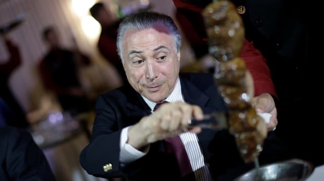 Temer schneidet demonstrativ Fleisch von einem Spiess und macht eine genüssliche Miene. Temer schneidet demonstrativ Fleisch von einem Spiess und macht eine genüssliche Miene.