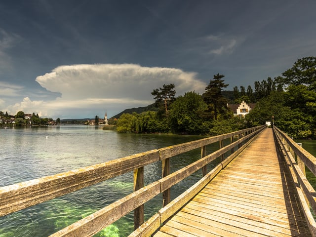 Eine ausgereifte Gewitterwolke mit weiss leuchtendem Amboss (oberer Teil der Wolke) steht über Stein am Rhein, im Vordergrund führt ein langer Holzsteg über den Fluss.