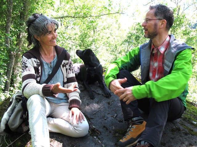 Eine Frau und ein Mann sitzen diskutierend auf einem Stein im Wald Eine Frau und ein Mann sitzen diskutierend auf einem Stein im Wald