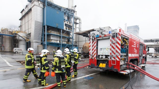 Feuerwehrleute mit Schläuchen im Einsatz, rechts das Feuerwehrauto Feuerwehrleute mit Schläuchen im Einsatz, rechts das Feuerwehrauto