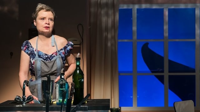 Rebecca steht an der Spüle, im Hintergrund ist durch das Fenster die Flosse eines Wals zu sehen. Rebecca steht an der Spüle, im Hintergrund ist durch das Fenster die Flosse eines Wals zu sehen.