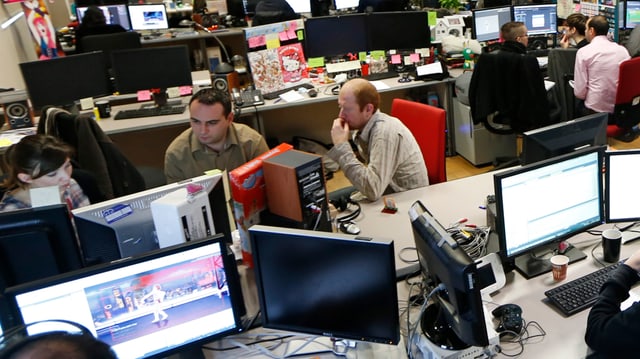 Mitarbeiter eines Unternehmens für Computerspiele sitzen zusammen vor grossen Bildschirmen. Mitarbeiter eines Unternehmens für Computerspiele sitzen zusammen vor grossen Bildschirmen.