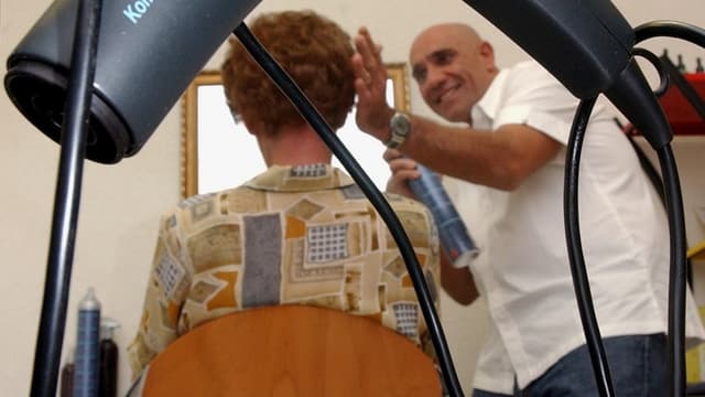 Coiffeur spräht etwas auf die Haare einer Kundin. Coiffeur spräht etwas auf die Haare einer Kundin.