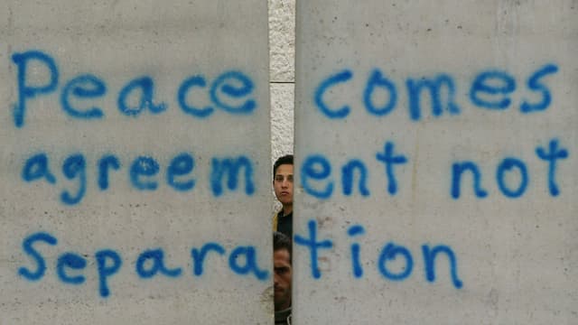 Zwei Jungen schauen hinter einer Mauer hervor auf der steht: "Peace comes agreement not Separation" Zwei Jungen schauen hinter einer Mauer hervor auf der steht: "Peace comes agreement not Separation"