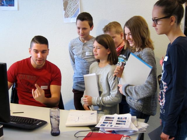 Ein Mann am Computer erklärt fünf Kindern etwas.