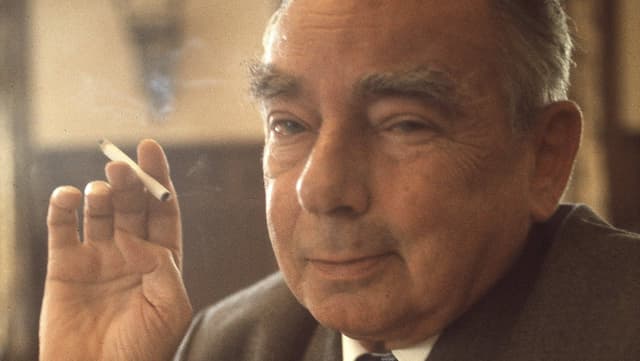 Erich Kästner mit einer brennenden Zigarette in der Hand schaut lächelnd in die Kamera Erich Kästner mit einer brennenden Zigarette in der Hand schaut lächelnd in die Kamera