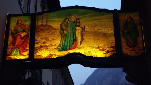 Das beleuchtete Transparent über einer Gasse in Mendrisio zeigt drei Frauen in grosser Trauer auf dem Kreuzigungshügel in Golgatha.