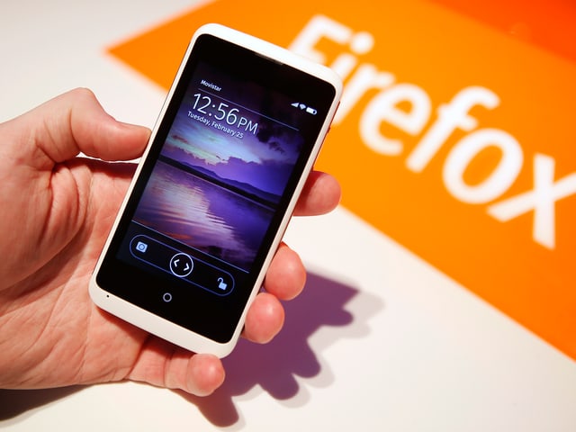 Eine Hand hält ein Smartphone auf dem Mozillas Betriebssystem Firefox OS läuft. Eine Hand hält ein Smartphone auf dem Mozillas Betriebssystem Firefox OS läuft.