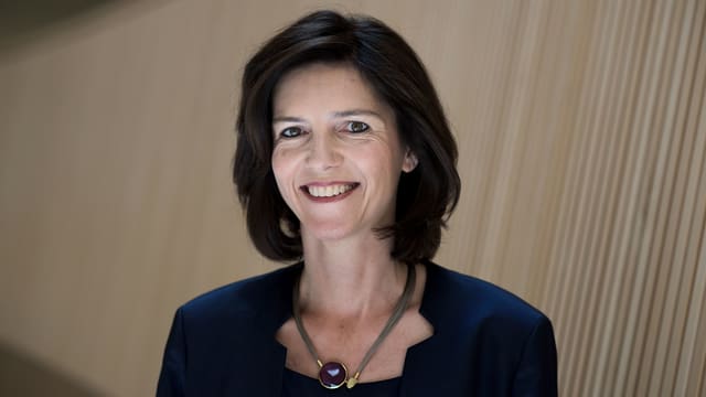 Eine Frau mit dunklem Haar, lächelnd vor einer schräg schraffierten Wand. Eine Frau mit dunklem Haar, lächelnd vor einer schräg schraffierten Wand.