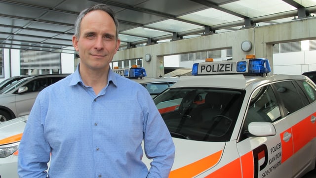 Mann in blauem Hemd vor Polizeiautos. Mann in blauem Hemd vor Polizeiautos.