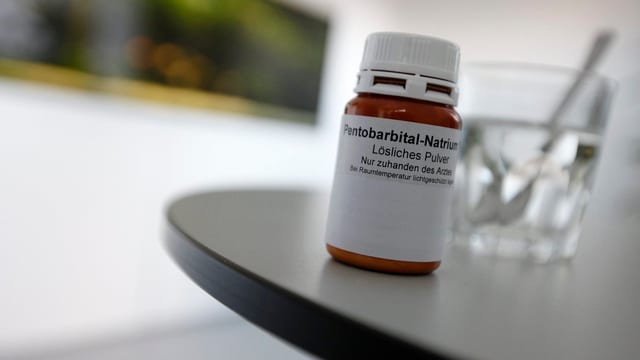 Symbolbild: Ein Schraubglas mit dem Medikament, daneben auf einem Tisch ein Glas Wasser mit Löffel. Symbolbild: Ein Schraubglas mit dem Medikament, daneben auf einem Tisch ein Glas Wasser mit Löffel.