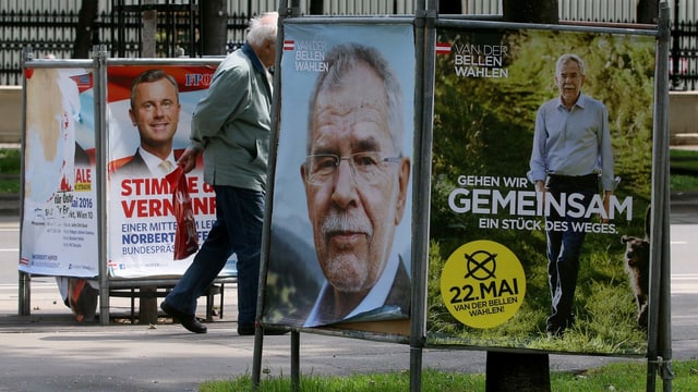 Ein Mann marschiert zwischen Wahlplakaten hindurch. Ein Mann marschiert zwischen Wahlplakaten hindurch.