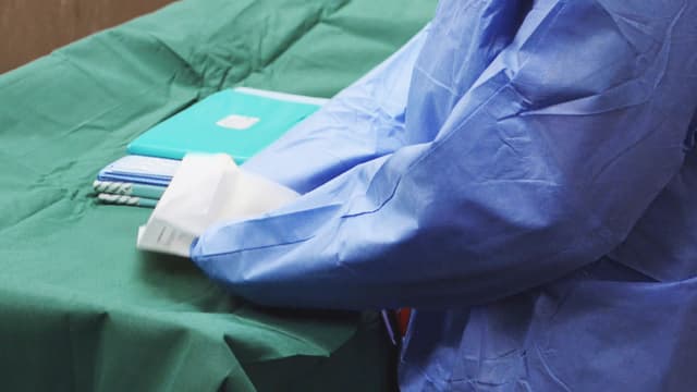 Eine Person in OP-Kittel packt sterile Instrumente aus. Eine Person in OP-Kittel packt sterile Instrumente aus.