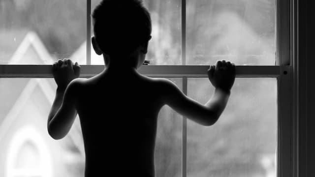 Kind von hinten, das vor einem geschlossenen Fenster steht. Kind von hinten, das vor einem geschlossenen Fenster steht.