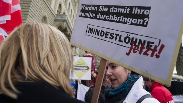 Eine Frau mit einem Transparent, das Mindestlöhne fordert. Eine Frau mit einem Transparent, das Mindestlöhne fordert.