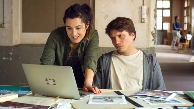 Ein Junge und eine Frau sitzen an einem Schreibtisch vor einem Laptop.