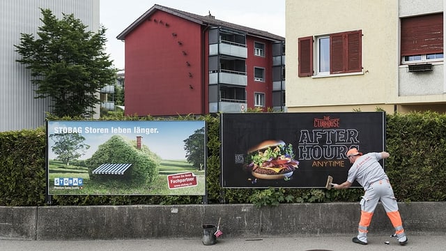 Ein Mann klebt neue Plakate auf zwei Plakatwände in einer städtischen Umgebung. Ein Mann klebt neue Plakate auf zwei Plakatwände in einer städtischen Umgebung.
