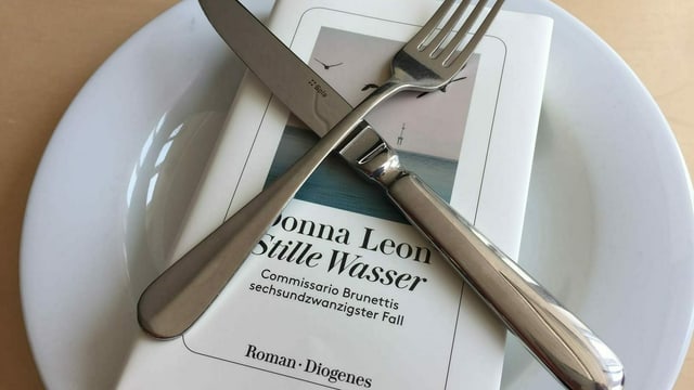 Der neue Krimi «Stille Wasser» von Donna Leon auf einem weissen Teller. Das Besteck gekreuzt darüber. Der neue Krimi «Stille Wasser» von Donna Leon auf einem weissen Teller. Das Besteck gekreuzt darüber.