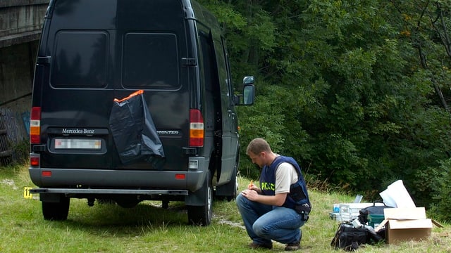 Polizist kniet neben schwarzem Transporter. Polizist kniet neben schwarzem Transporter.