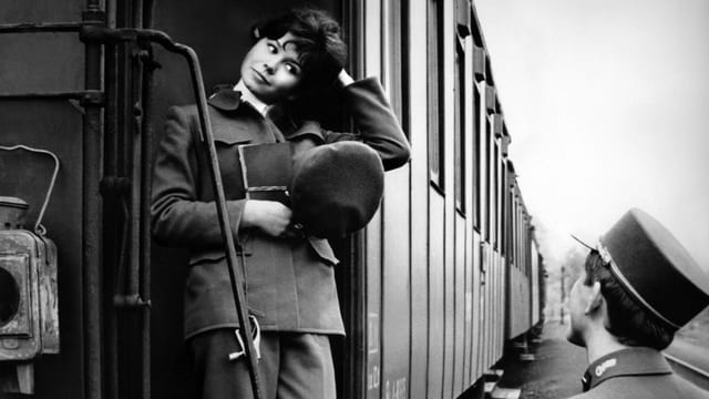 Filmstill: Ein Schaffner blickt zu einer Dame hoch, die auf einem Waggon steht. Filmstill: Ein Schaffner blickt zu einer Dame hoch, die auf einem Waggon steht.