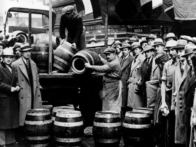 Schwarzweissfoto: Ein Laster mit Fässern wird entladen, viele Schaulustige stehen daneben. Schwarzweissfoto: Ein Laster mit Fässern wird entladen, viele Schaulustige stehen daneben.
