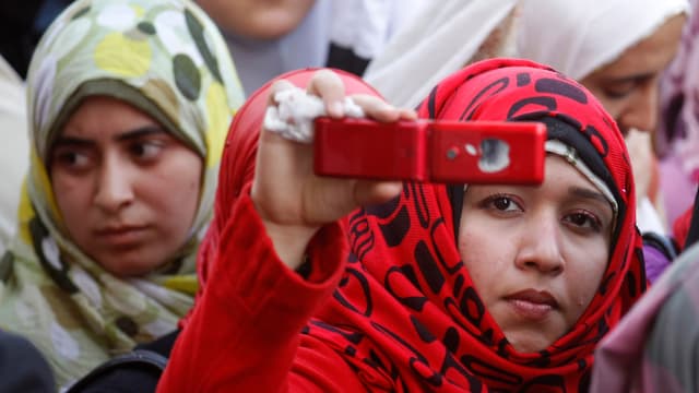 Zwei junge Frauen mit Kopftuch, die eine hält ihr Handy hoch und fotografiert Zwei junge Frauen mit Kopftuch, die eine hält ihr Handy hoch und fotografiert