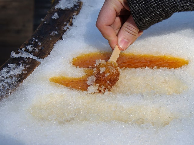 Schnee, auf welchem orange Streifen liegen. Eine Hand wickelt einen solchen Streifen um ein Hölzchen. Schnee, auf welchem orange Streifen liegen. Eine Hand wickelt einen solchen Streifen um ein Hölzchen.