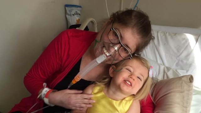 Frau mit Atemmaske und kleinem Kind im Bett Frau mit Atemmaske und kleinem Kind im Bett