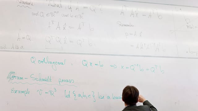 Hier sieht man viel weisse Wand mit darauf geschriebenen Formeln. Am unteren Bildrand ist ein Professor, der eben diese Formeln auf der weissen Wand notiert. Hier sieht man viel weisse Wand mit darauf geschriebenen Formeln. Am unteren Bildrand ist ein Professor, der eben diese Formeln auf der weissen Wand notiert.