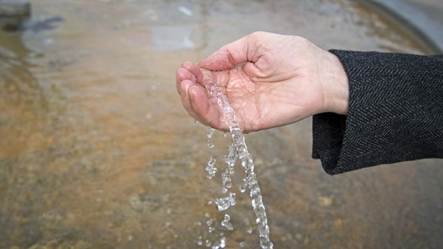 Ein Wasserstrahl spritzt auf eine Hand. 