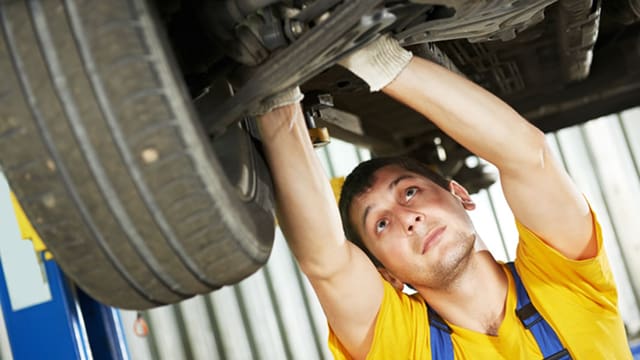 Ein Garagist steht unter einem angehobenen Auto und repariert eine Achse. Ein Garagist steht unter einem angehobenen Auto und repariert eine Achse.