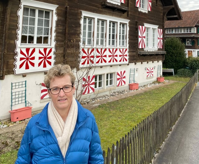 Frau in kobaltblauer Stepjacke steht vor Bauernhaus. Frau in kobaltblauer Stepjacke steht vor Bauernhaus.