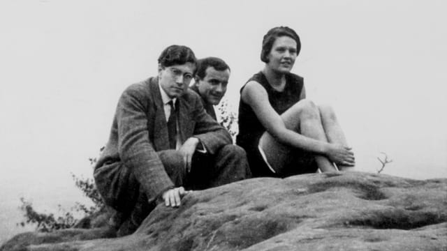 Zwei Männer und eine Frau sitzen auf einem Felsen.