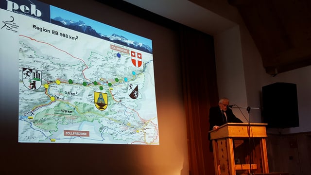 Da vart dretga vesan ins ina carta da geografia cun la regiun Engiadina Bassa, da vart sanestra discurra il vegl president Guido Paolini Da vart dretga vesan ins ina carta da geografia cun la regiun Engiadina Bassa, da vart sanestra discurra il vegl president Guido Paolini