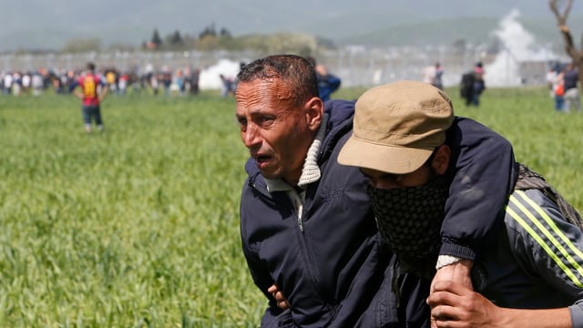 Ein sichtlich angeschlagener, älterer Mann wird von einem jüngeren Flüchtling vom Grenzzaun weggebracht. Ein sichtlich angeschlagener, älterer Mann wird von einem jüngeren Flüchtling vom Grenzzaun weggebracht.