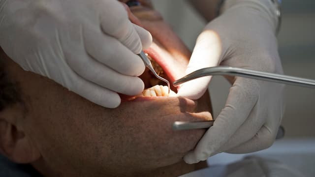 Ein Mann liegt mit aufgesperrtem Mund auf einem Zahnarztstuhl und wird behandelt.