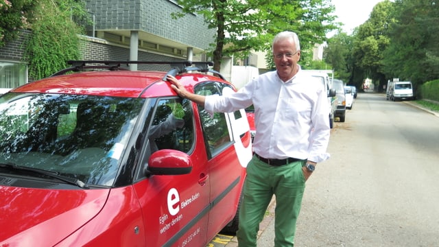 Ein Mann steht bei einem roten Auto. Ein Mann steht bei einem roten Auto.
