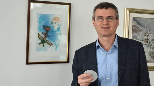 Ein Mann mit Brille hält ein Silikon-Teil in der Hand. Ein Mann mit Brille hält ein Silikon-Teil in der Hand.