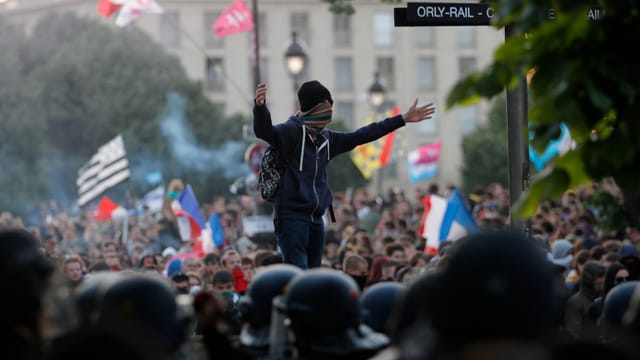Ein vermummter Demonstrant steht über der Menschenmenge mit ausgebreiteten Armen. Ein vermummter Demonstrant steht über der Menschenmenge mit ausgebreiteten Armen.