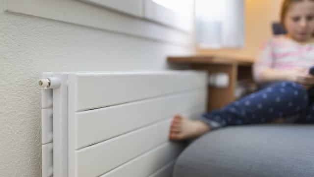 Mädchen im Hintergrund wärmt ihre Füsse an einem Heizkörper Mädchen im Hintergrund wärmt ihre Füsse an einem Heizkörper