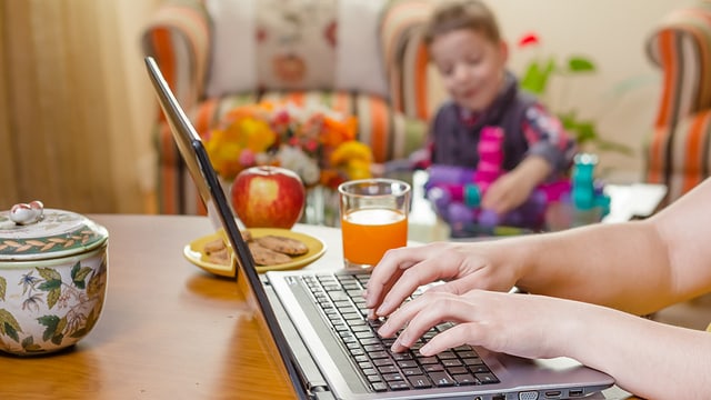 Frau am Computer, im Hintergrund ein spielendes Kind Frau am Computer, im Hintergrund ein spielendes Kind