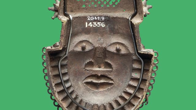 Eine Maske aus grauem Material. Sie zeigt ein Gesicht mit einer Art Bart. Eine Maske aus grauem Material. Sie zeigt ein Gesicht mit einer Art Bart.