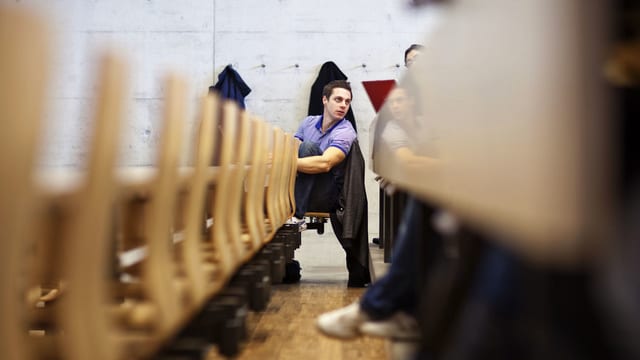 Ein Student sitzt in einem modernen Hörsaal und spricht mit einem nicht sichtbaren Nachbarn. Ein Student sitzt in einem modernen Hörsaal und spricht mit einem nicht sichtbaren Nachbarn.