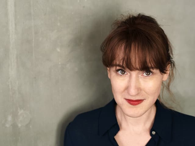 Porträtfoto der Autorin Nora Bossong vor einer grauen Wand. Porträtfoto der Autorin Nora Bossong vor einer grauen Wand.